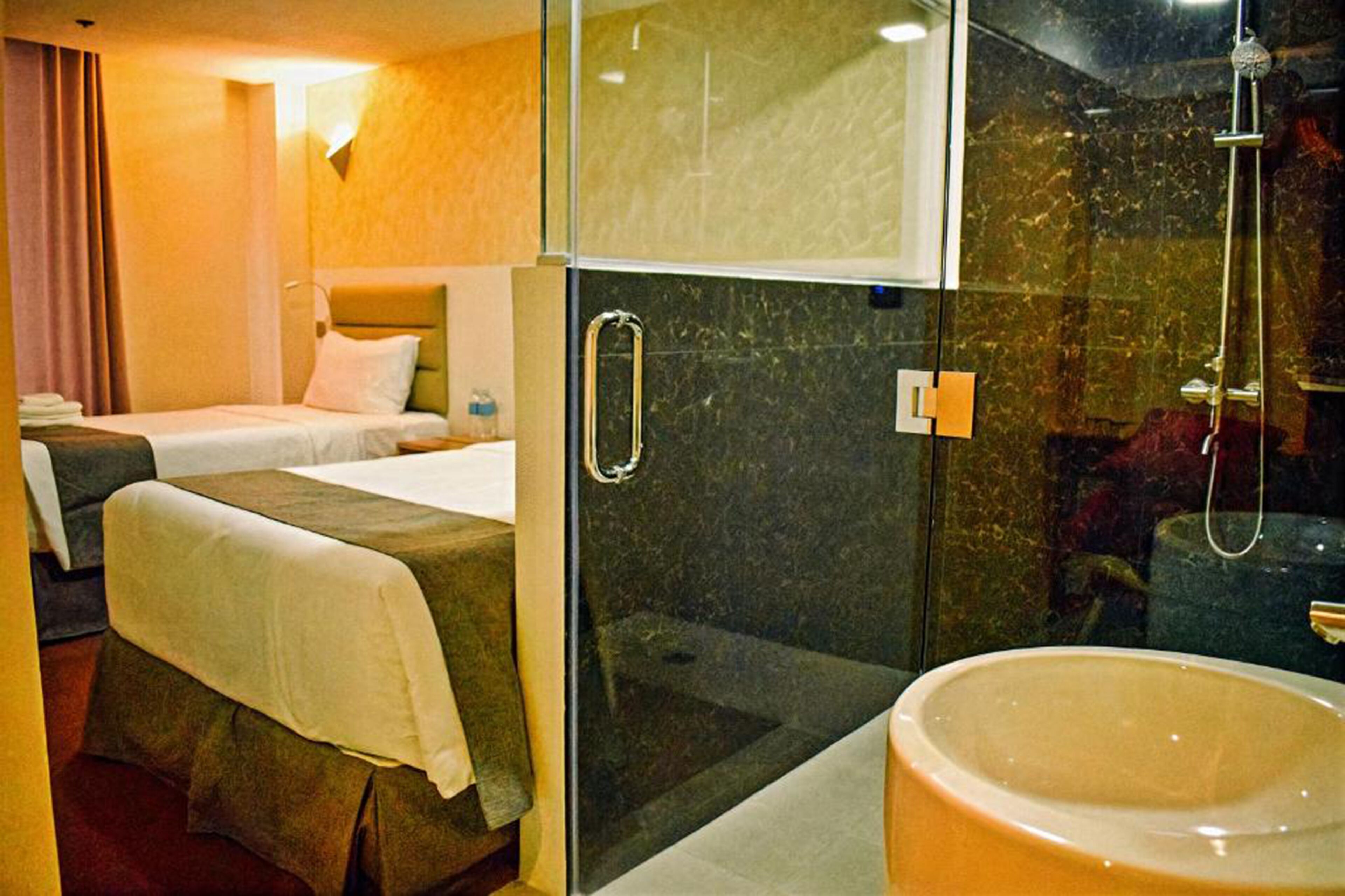 Een hotelkamer met twee bedden, een douchecabine van glas en een ruime badkuip.