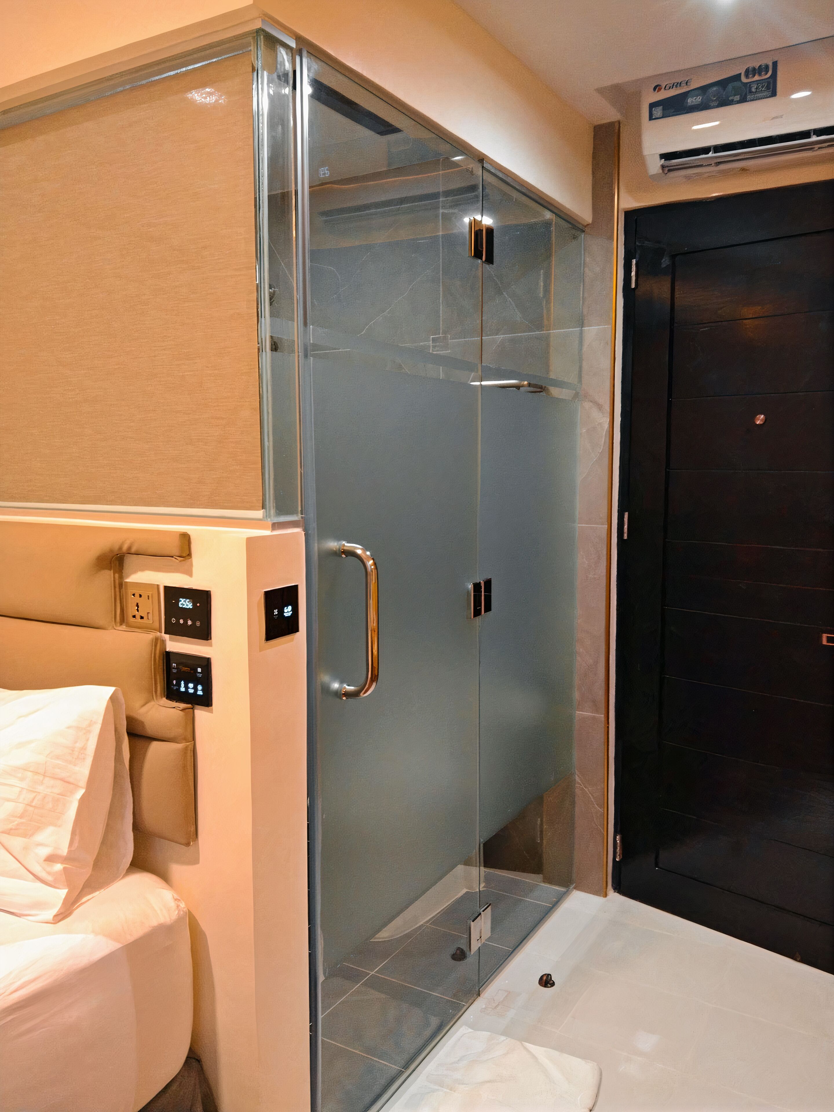 A modern bathroom with a glass shower enclosure, a control panel, and a dark door.