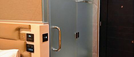 A modern bathroom with a glass shower enclosure, a control panel, and a dark door.