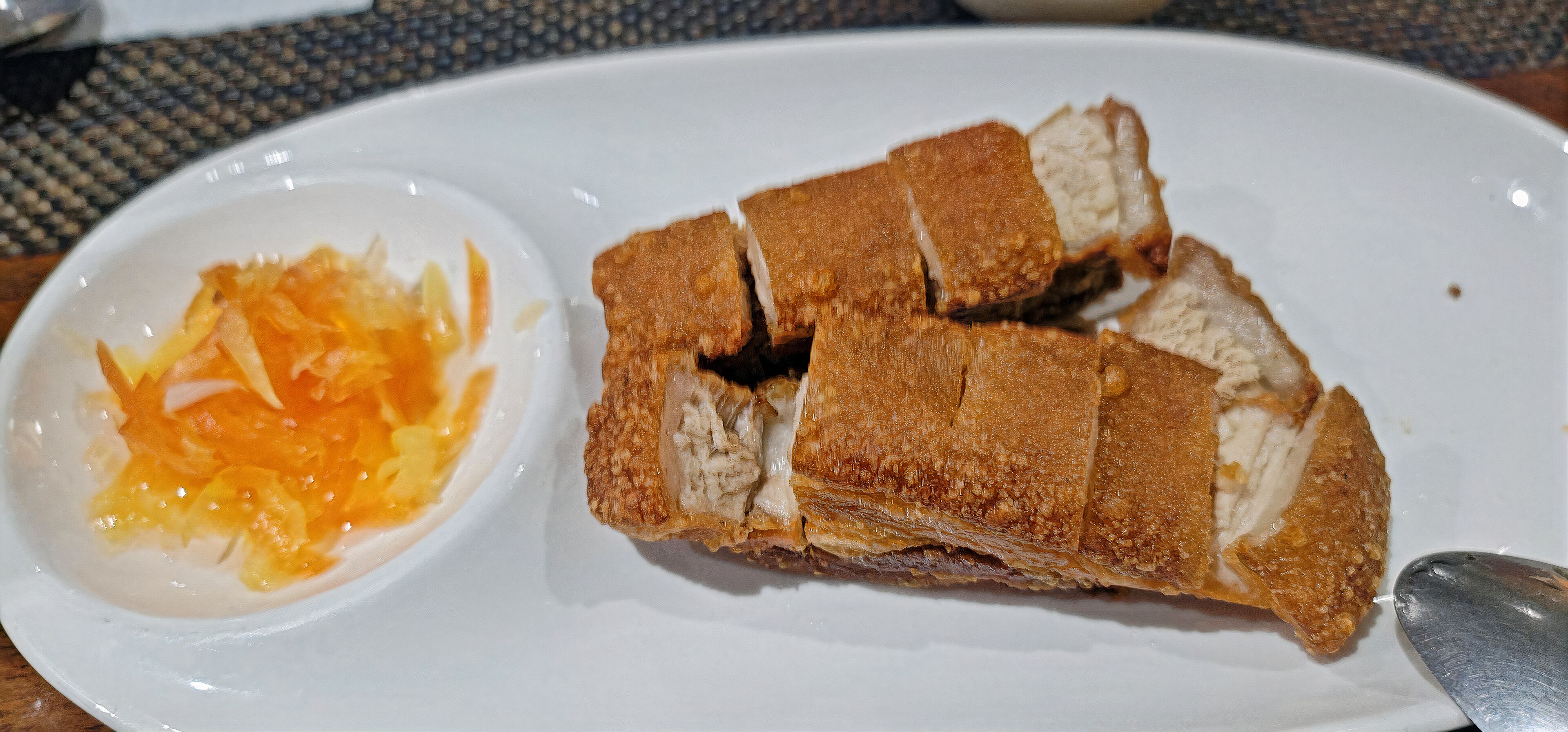 A plate with a piece of roasted meat and a small bowl of sauce.