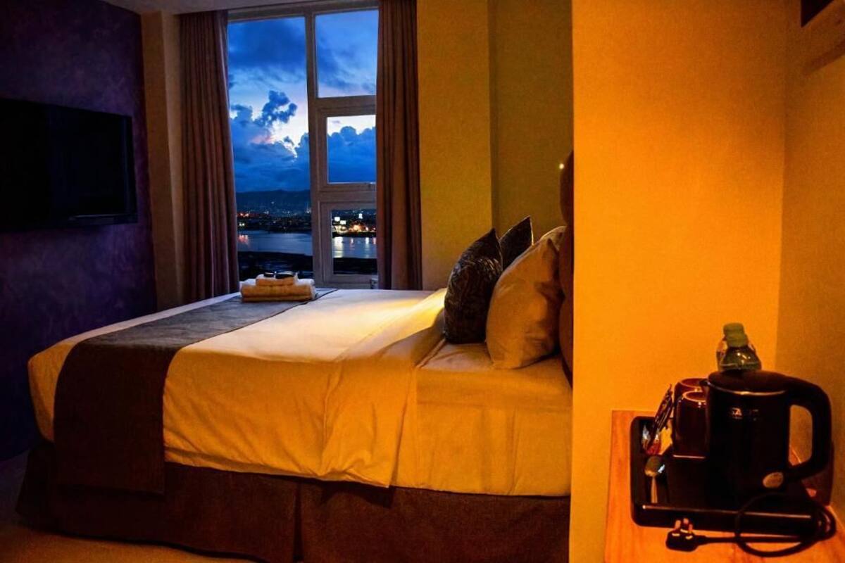 Une chambre d’hôtel avec un lit, une fenêtre donnant sur la ville, une machine à café et un plateau avec une bouteille et des verres.