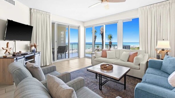 A spacious living room with a large TV, a sofa, a coffee table, and a view of the ocean. - Modern Coastal Retreat Near Miramar Beach With EV Charging Capablities (Destin)