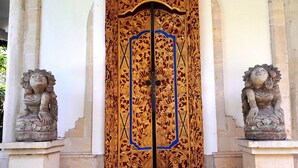 A wooden door with intricate carvings and two lion statues on either side. - Panorama Hotel Ubud (Ubud)