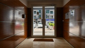 Entrada de hotel con interior de madera, puerta de cristal que da al exterior y suelo de baldosas.