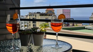 Dos copas de vino tinto sobre una mesa de balcón con una planta en maceta y un cubo de metal.