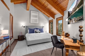 A bedroom with a bed, bedside table, lamp, books, and a painting.