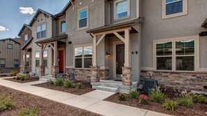 A two-story house with a stone facade, multiple windows, and a front porch. - Luxury Townhome at Wasatch Springs - Black Rock Ridge + Ski Park City (Heber City)