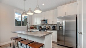 A modern kitchen with white cabinets, stainless steel appliances, a large island with bar stools, and pendant lighting. - Luxury Townhome at Wasatch Springs - Black Rock Ridge + Ski Park City (Heber City)