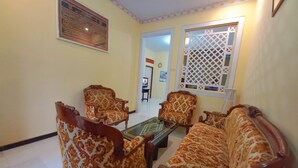 A living room with patterned sofas and armchairs, a coffee table, and a television in the background. - Rumah Kost Nakula (Banyuwangi)