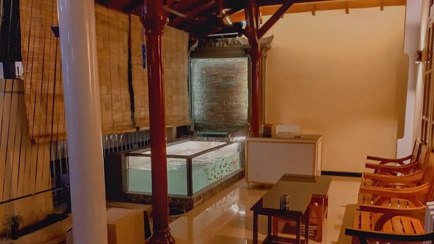 A spacious room with a large column, a wooden ceiling, and a seating area with wooden chairs. - Rumah Kost Nakula (Banyuwangi)