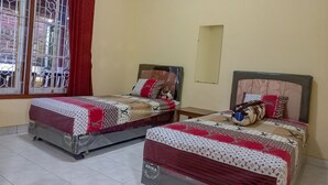 A hotel room with two beds, a window with a view, and an air conditioning unit on the wall. - Rumah Kost Nakula (Banyuwangi)