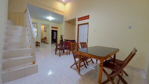 A spacious living area with a dining table, chairs, a staircase, and a door leading to another room. - Rumah Kost Nakula (Banyuwangi)
