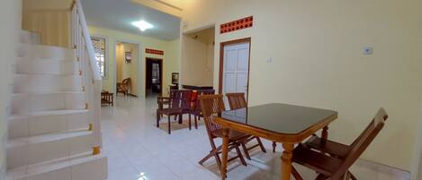 A spacious living area with a dining table, chairs, a staircase, and a door leading to another room.