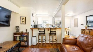 Ett kompakt bostadsutrymme med ett köksområde, en sittgrupp med en lädersoffa och en bokhylla.