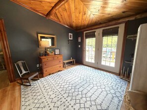 A room with a wooden ceiling, a dresser, a mirror, and a patterned rug. - Ligonier Creekside Cabin in Laurel Highlands (Ligonier)