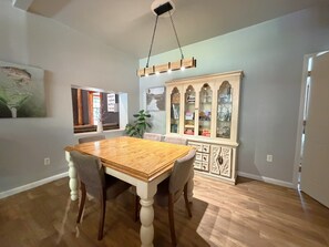 Uma sala de jantar com mesa e cadeiras de madeira, um aparador com portas de vidro e obras de arte nas paredes.