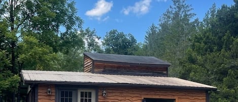 A rustic cabin with a wooden deck, a chimney, and a large window.