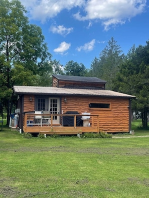 Une cabane rustique dotée d’une terrasse en bois, d’une cheminée et d’une grande fenêtre.