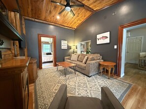 A living room with a wooden ceiling, a sofa, a coffee table, and a rug. - Ligonier Creekside Cabin in Laurel Highlands (Ligonier)