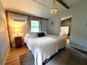 Um quarto com uma cama grande, uma mesinha de cabeceira com abajur, uma janela com cortinas e um lustre.