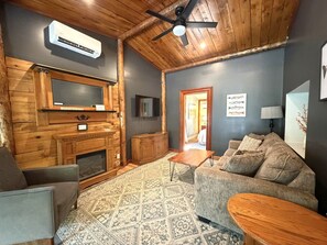 A cozy living room with a fireplace, a television, and a ceiling fan.