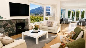 Un salon moderne avec une cheminée en pierre, un téléviseur à écran plat, un canapé, une table basse et une vue sur un paysage montagneux.
