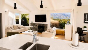 Un salon moderne doté d’un îlot de cuisine, d’une cheminée et d’une grande fenêtre offrant une vue sur les montagnes.
