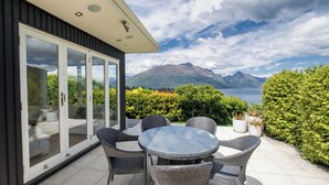 Une terrasse extérieure moderne, dotée d’une porte vitrée donnant accès à une salle de bain privative, de meubles en osier et offrant une vue panoramique sur les montagnes.