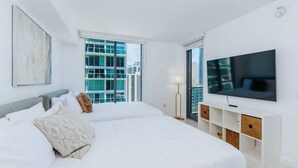 A modern bedroom with a large bed, a flat-screen TV, and a city view.
