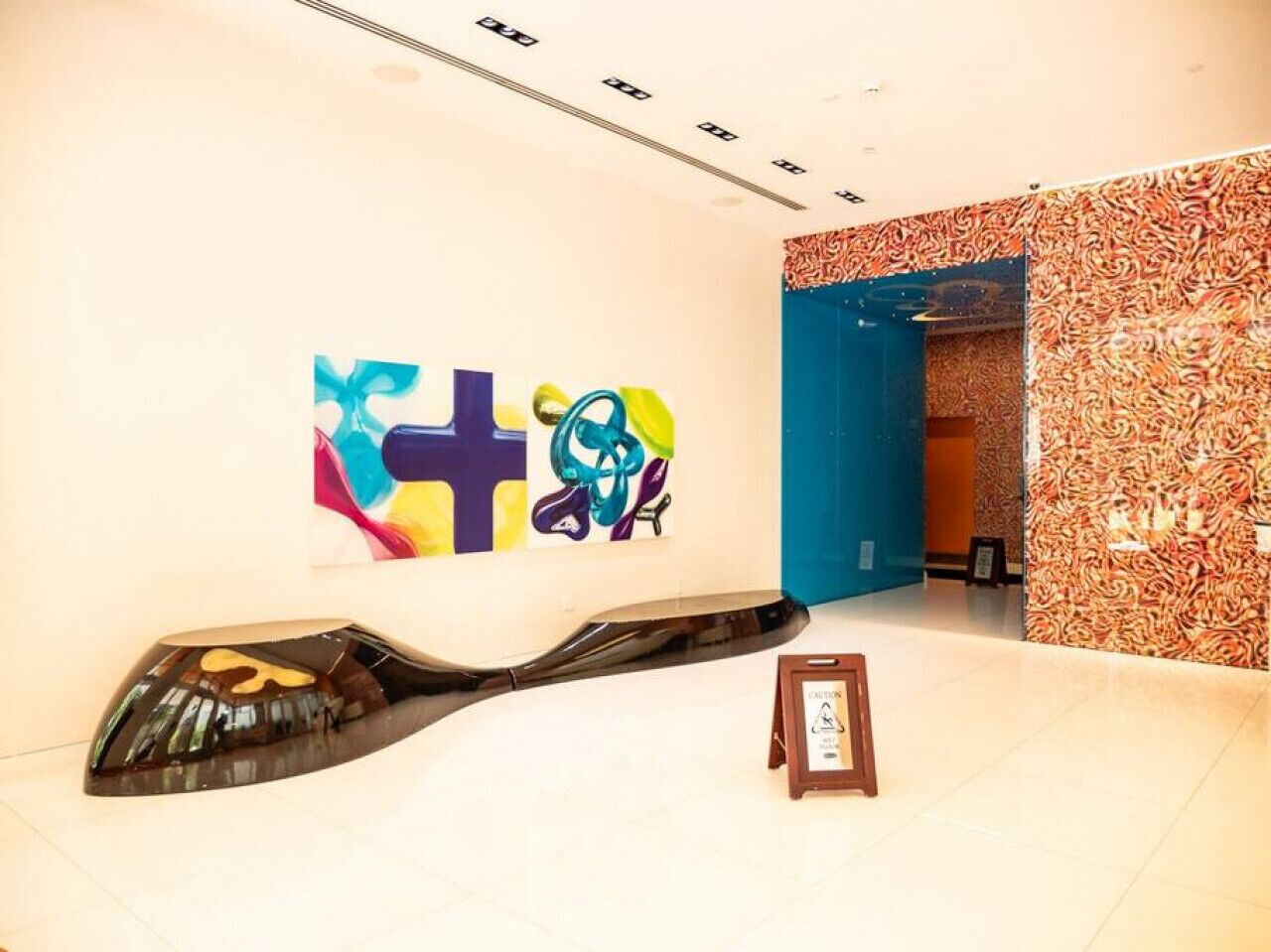 A hallway with a modern art installation, a blue door, and a caution sign.