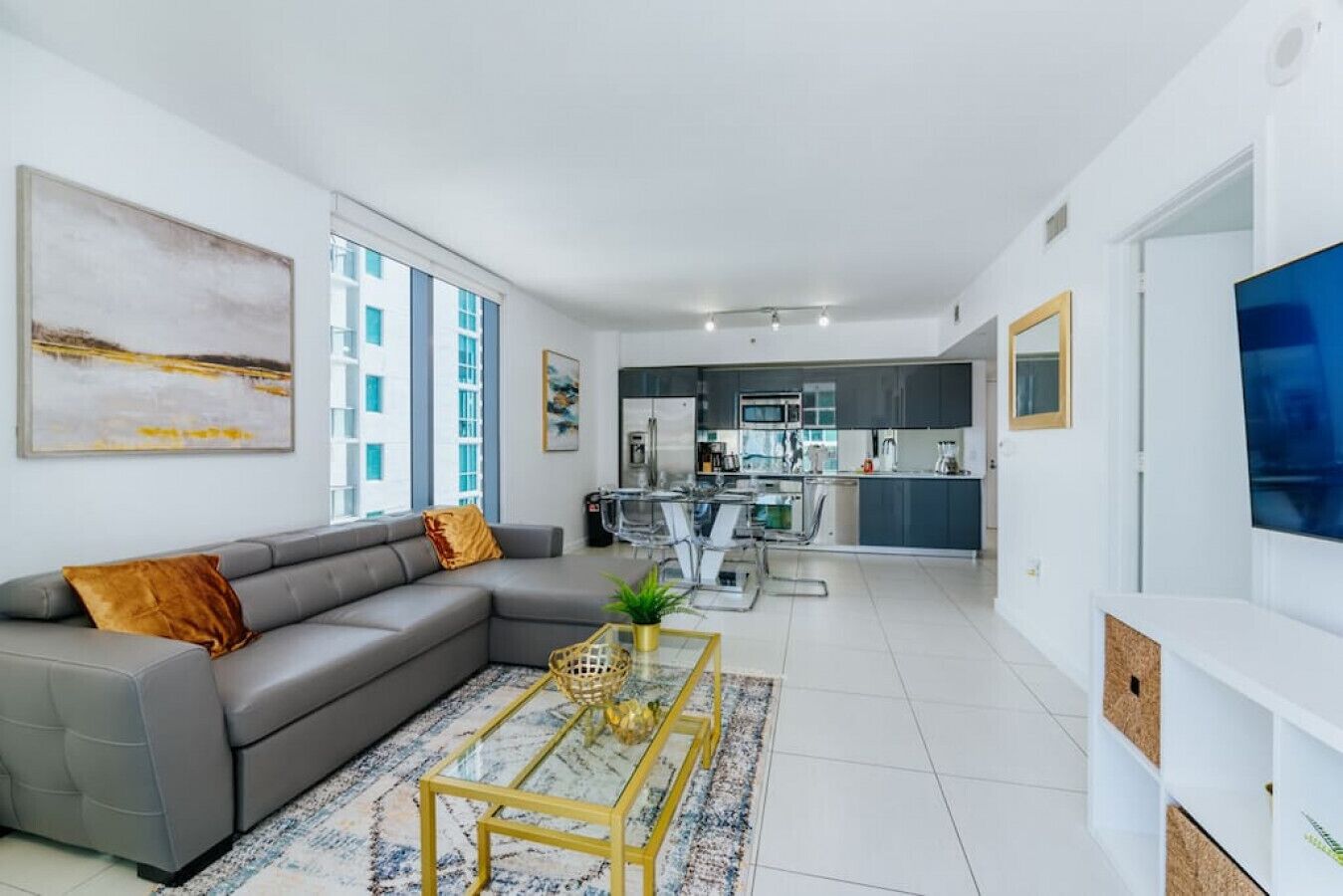 A modern living room with a grey sectional sofa, a glass coffee table, and a large TV on the right.