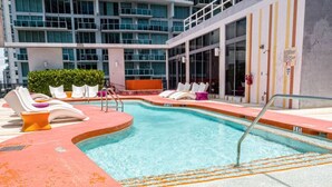 A swimming pool with lounge chairs and a glass-enclosed building in the background.