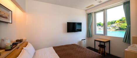 Habitación de hotel con cama, escritorio, silla, televisión y ventana con vistas al agua y vegetación.