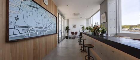 Un interior moderno con un mapa grande en la pared, una zona de bar con taburetes y ventanas amplias que ofrecen vistas.
