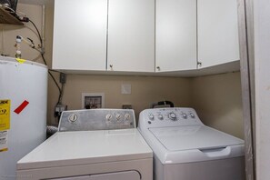 A laundry room with two washers and a dryer, a water heater, and a cabinet above.
