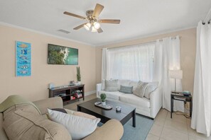 A living room with a sofa, coffee table, ceiling fan, and artwork on the wall. - Bayfront Unit | Dock & Bay Views | Siesta Key (Sarasota)