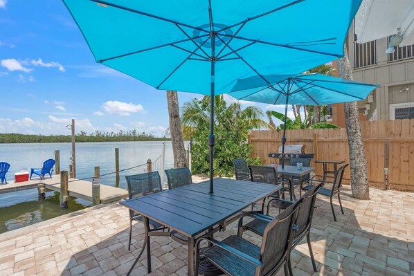 An outdoor patio with a table and chairs, a grill, and a view of the water.