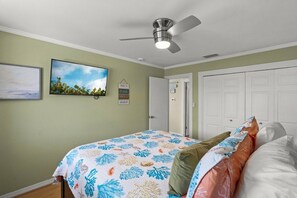 A bedroom with a bed, a ceiling fan, a door, and a wall-mounted TV.