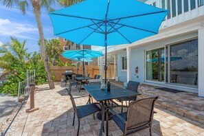 An outdoor patio with tables and chairs, blue umbrellas, and a wooden fence.