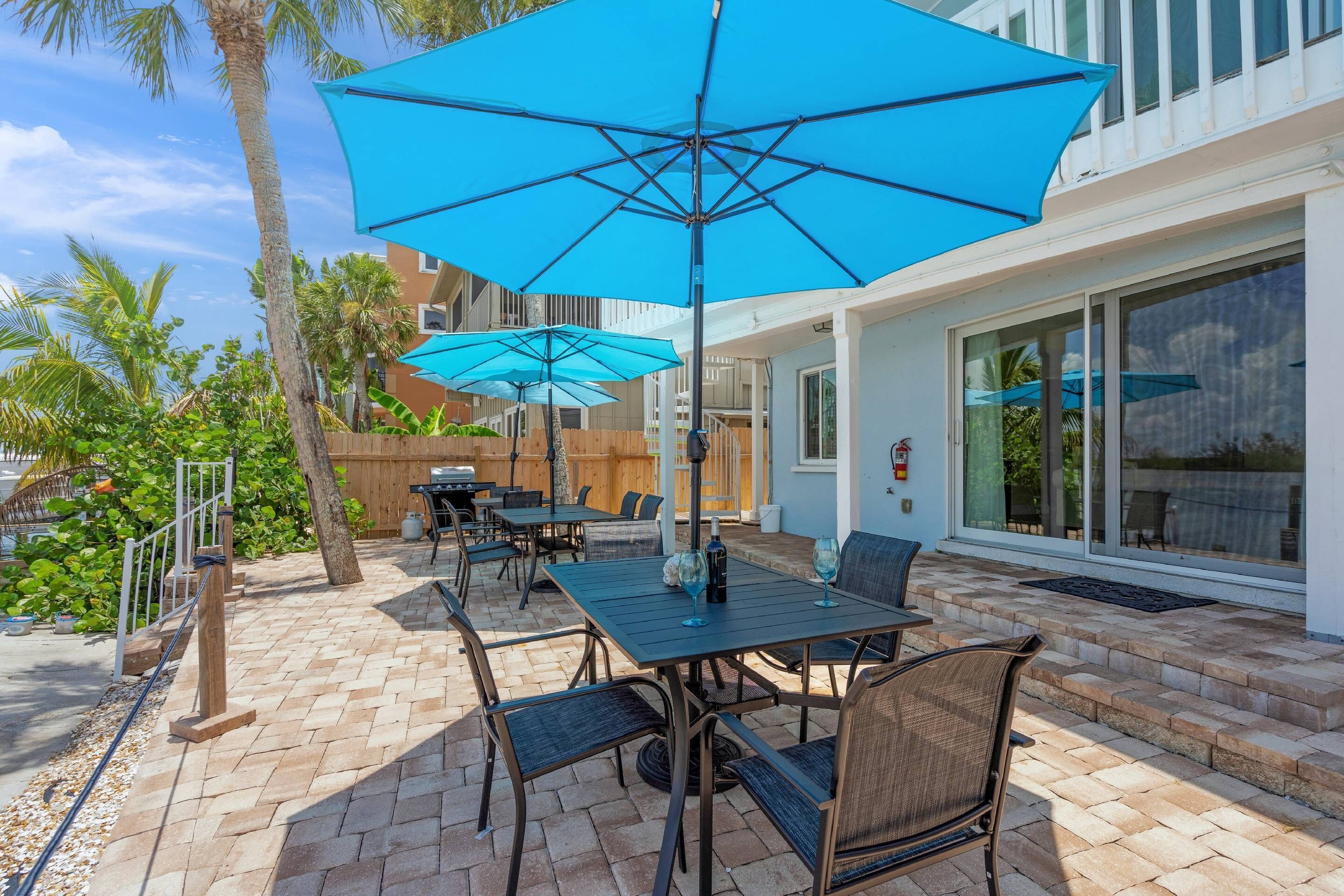 An outdoor patio with tables and chairs, blue umbrellas, and a wooden fence.
