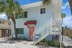 A two-story building with a red awning, a staircase, and a gated entrance. - Siesta Key | Bay Patio & Dock | Free Activities (Sarasota)