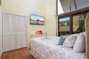 A bedroom with a bed, a nightstand, a painting, and a window with a view of a building. - Cozy Cottage on the Beach | Steps to SK Village (Siesta Key)