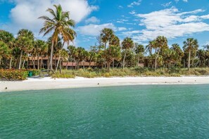 A beach with clear turquoise water, palm trees, and a building with a red roof. - Cozy Cottage on the Beach | Steps to SK Village (Siesta Key)