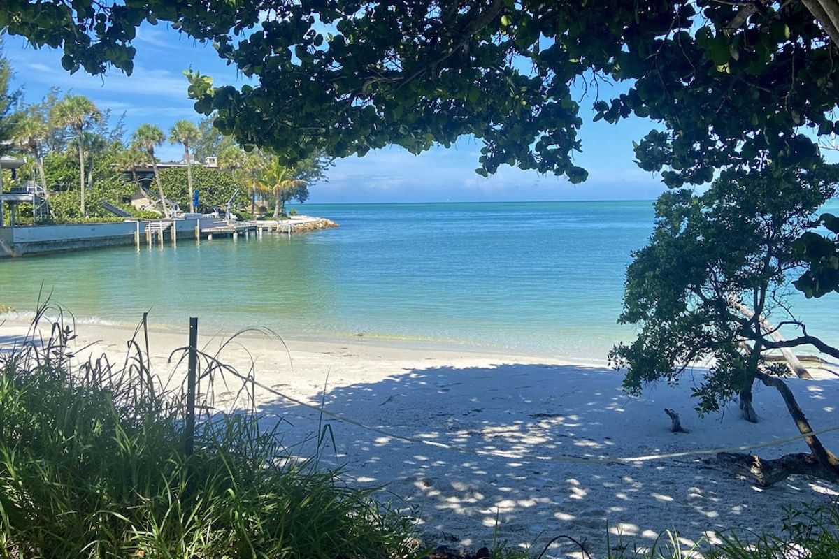 A beach with clear water, a sandy shore, and a dock.