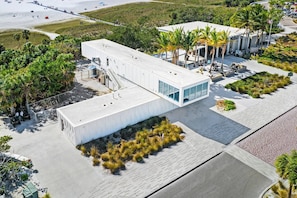 Un bâtiment moderne doté d’un toit plat, de grandes fenêtres et d’un espace extérieur couvert aménagé avec des sièges.