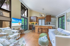 A spacious living area with a kitchen, a large window, and a television. - Cozy Cottage on the Beach | Steps to SK Village (Siesta Key)