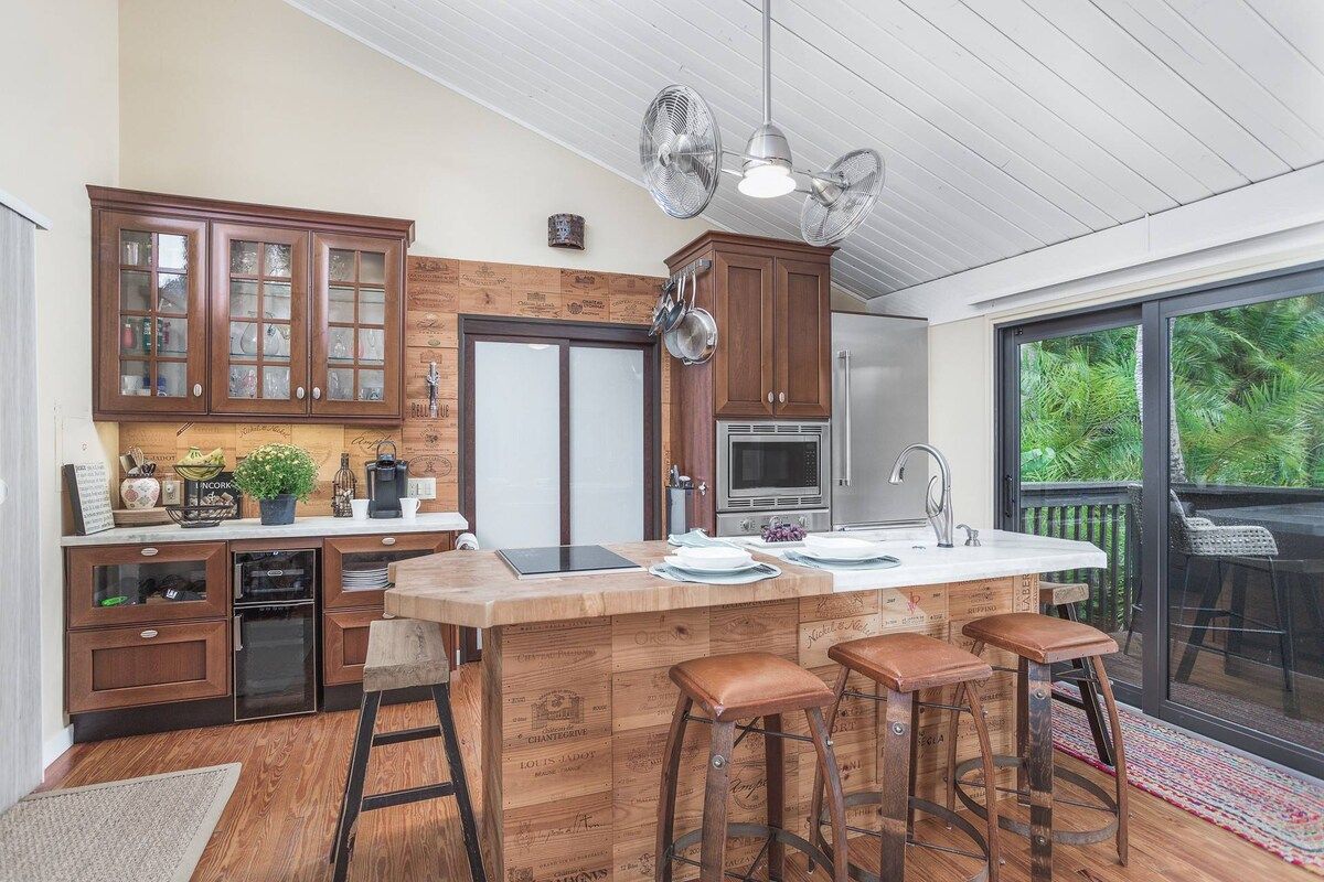 Een keuken met houten kasten, een centraal eiland met krukken en een schuifpui naar een balkon.