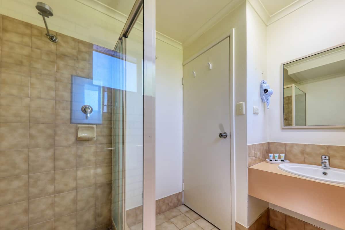A bathroom with a glass shower enclosure, a sink with toiletries, and a mirror.