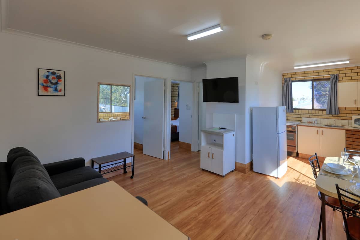 A modern living room with a sofa, a dining table, and a kitchen area with a TV, refrigerator, and wooden cabinets.