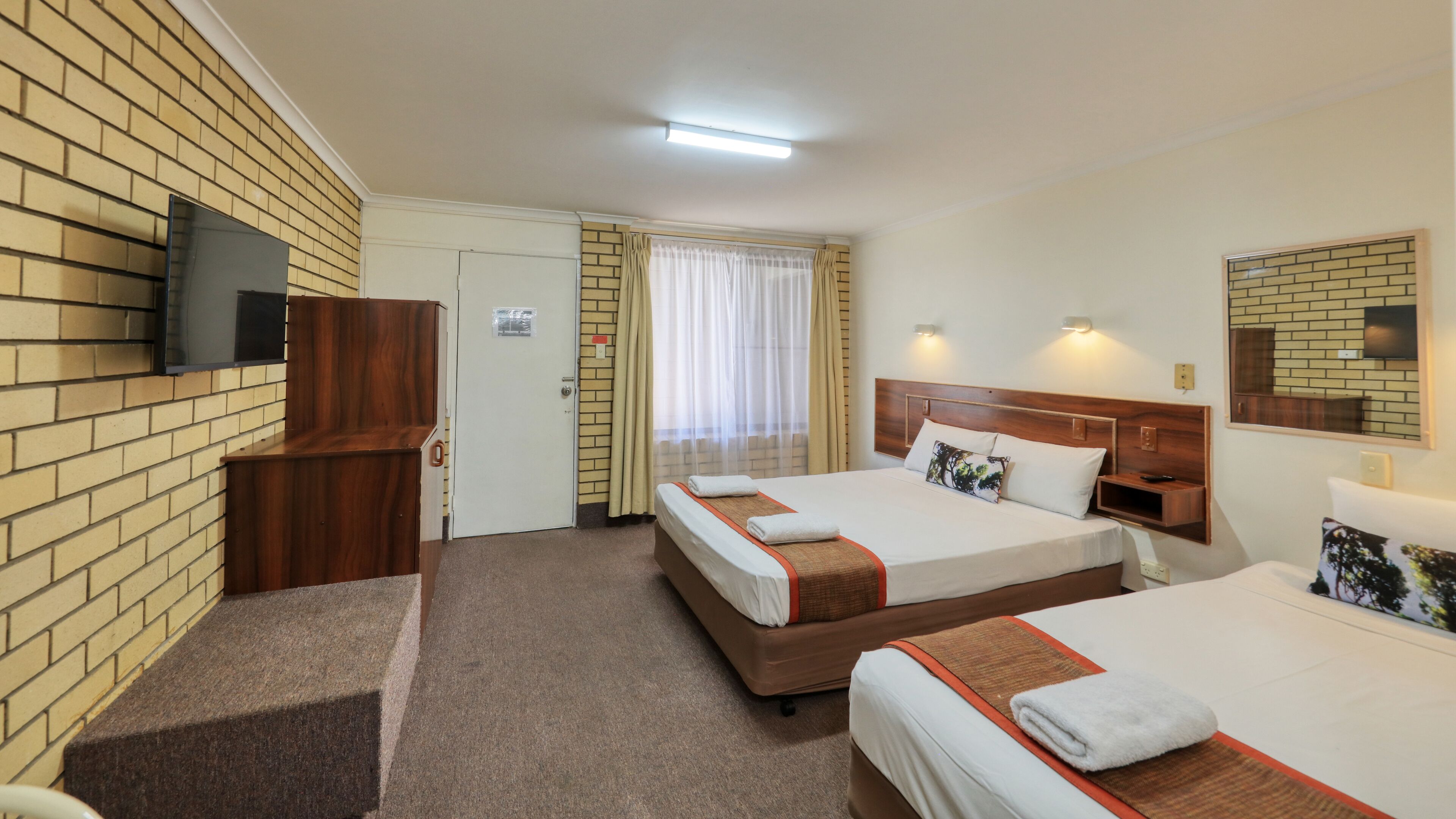 Une chambre d’hôtel avec deux lits, un téléviseur fixé au mur, un bureau en bois et une porte avec une pancarte.